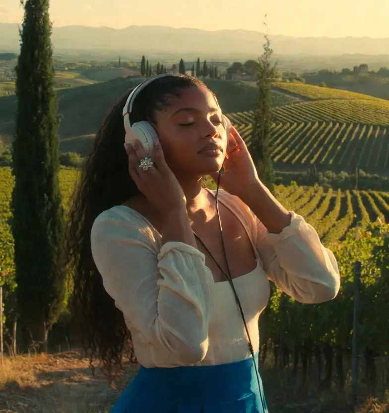Femme avec boucles d’oreilles écoutant de la musique avec un casque audio en Toscane Italie, ambiance romantique et ensoleillée inspirée de You, Me & Tuscany (Toi, moi et la Toscane) (2026) avec Halle Bailey et Regé-Jean Page, bande originale et musique du trailer Escapade de Janet Jackson
